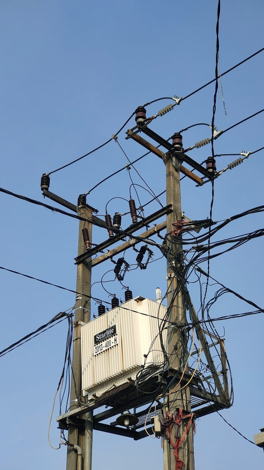 Electrical transformer and utility power lines against a clear blue sky